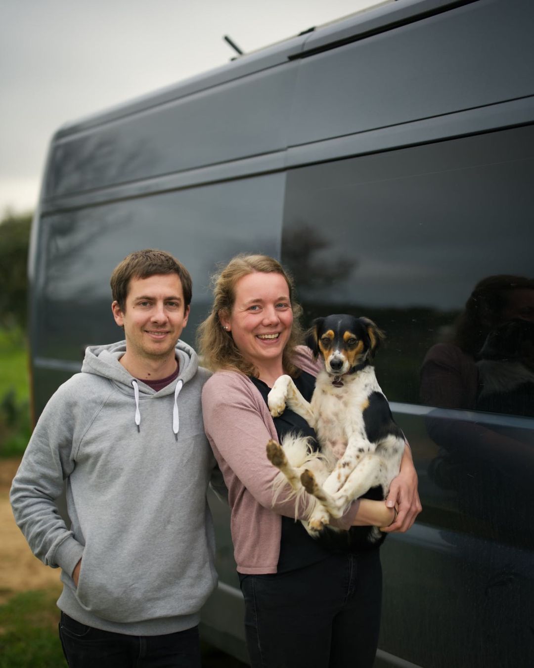 Zwei Menschen mit Hund vor ihrem Van